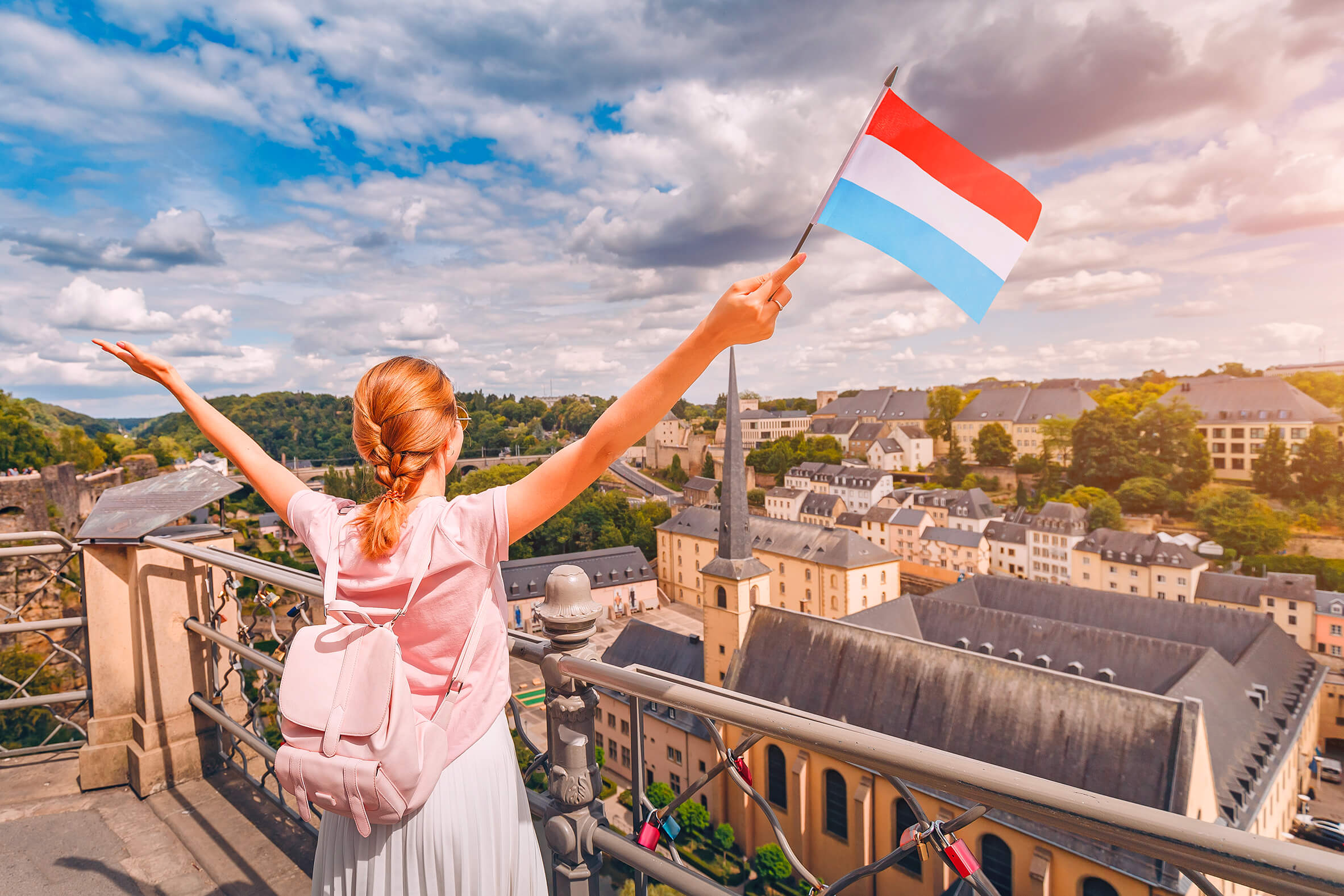 Woman raising her hands holding a Luxembourg flag in front of Neimënster Abbey